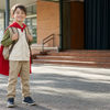 Child wearing a red cape and carrying a backpack outside a school assembly hall