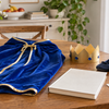 Blue child-sized cape, crown, soft shoes and a plain closed book on a family table