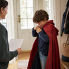 Child fastening a plain cape in a family entryway with an adult nearby