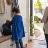 Child wearing a plain blue cape and checking a school backpack at home