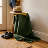 Ordinary black child-size school shoes beside a green cape and explorer hat at a home entryway