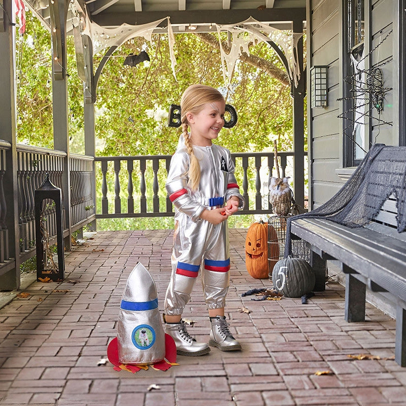 Child wearing silver astronaut costume with rocket backpack standing against white background